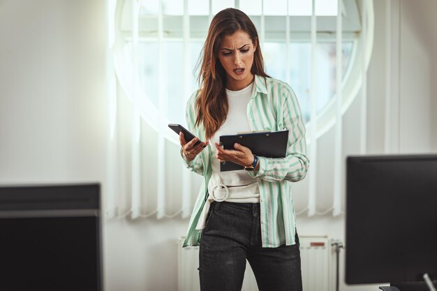 Une jeune femme d'affaires sérieuse et pensive travaille au bureau. Elle est surprise de quelque chose qu'elle regarde sur le document papier.