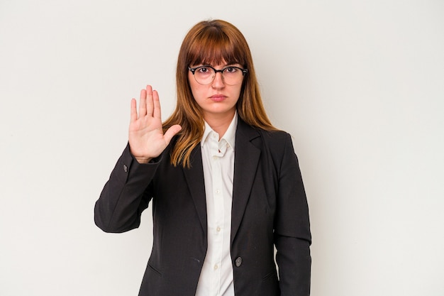 Jeune femme d'affaires sinueuse caucasienne isolée sur fond blanc debout avec la main tendue montrant un panneau d'arrêt, vous empêchant.