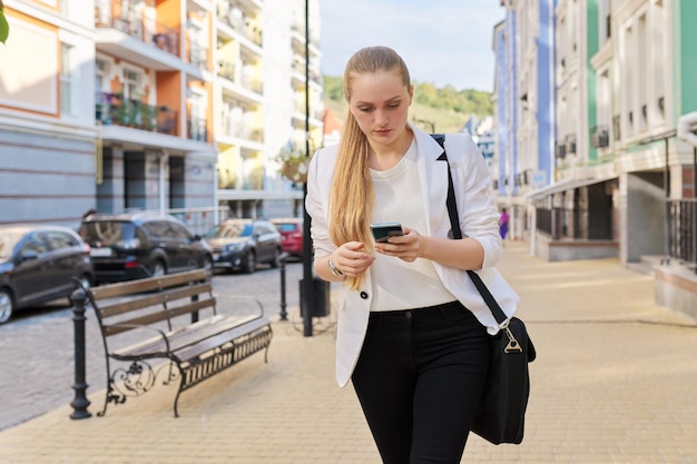 Jeune femme d'affaires avec smartphone marchant le long de la rue de la ville, femme lisant un message texte, regardant un e-mail