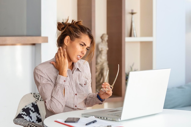 Jeune femme d'affaires souffrant de maux de cou massant son cou alors qu'elle était assise sur son lieu de travail au bureau à domicile