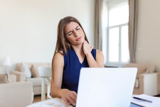 Jeune femme d'affaires souffrant de maux de cou se sentant fatiguée et stressée Jeune femme frustrée souffrant de douleurs au cou massant son cou alors qu'elle était assise sur son lieu de travail au bureau à domicile