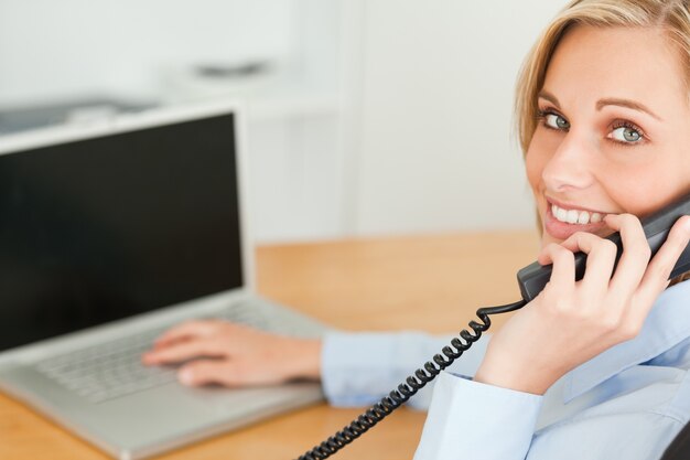 Jeune femme d&#39;affaires, souriant à la caméra pendant que vous êtes au téléphone