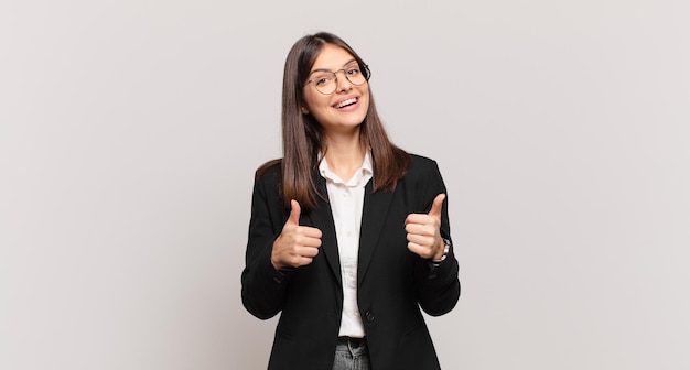 Jeune femme d'affaires souriant largement à la recherche de confiance positive positive et réussie avec les deux pouces vers le haut