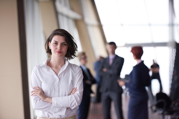 Une jeune femme d'affaires souriante devant son équipe estompée en arrière-plan. Groupe de jeunes entrepreneurs. Intérieur de bureau de démarrage moderne et lumineux.