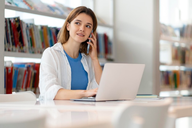 Jeune femme d'affaires souriante parlant sur un téléphone portable à l'aide d'un ordinateur portable travaillant en ligne