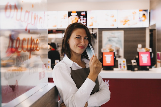 Photo une jeune femme d'affaires souriante en tablier se tient dans un café devant une vitrine, les bras croisés, regardant la caméra.