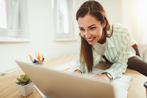 Jeune femme d'affaires souriante travaille sur ordinateur au bureau. Elle regarde quelque chose sur l'ordinateur portable.