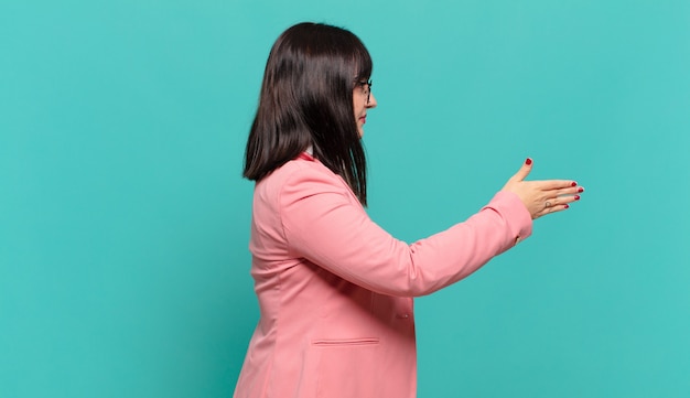 Jeune femme d'affaires souriante, vous saluant et offrant une poignée de main pour conclure un accord réussi, concept de coopération