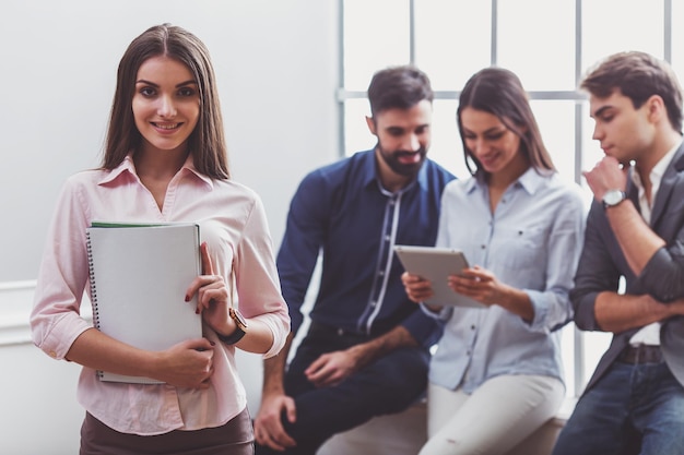 Jeune femme d'affaires tenant un ordinateur portable en arrière-plan trois hommes d'affaires avec une tablette à la main assis sur le rebord de la fenêtre