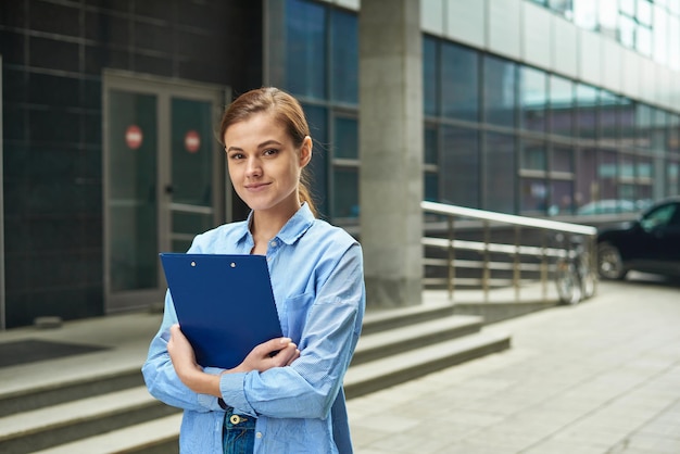 Jeune femme d'affaires tenant une tablette avec des documents à portée de main et regardant la caméra en souriant