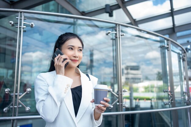 Photo jeune femme d'affaires tenant une tasse de café chaud et utilisant un smartphone en marchant dans la ville