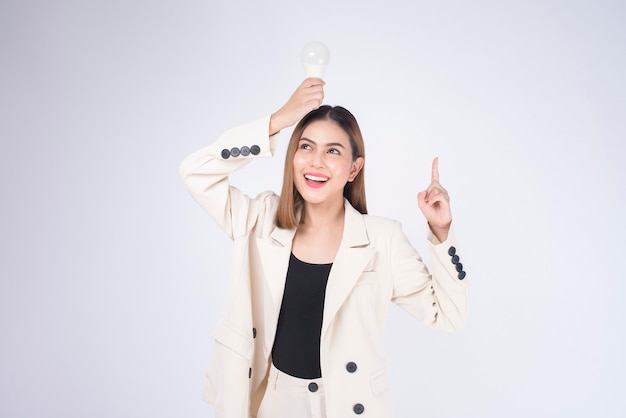 Une jeune femme d'affaires tient une ampoule portant un costume sur fond blanc studio