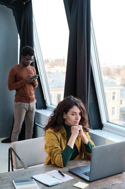 Jeune femme d'affaires travaillant sur ordinateur avec un homme debout en arrière-plan, ils travaillent au bureau