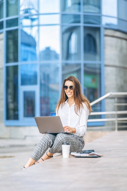 Jeune femme d'affaires travaillant sur l'ordinateur portable à l'extérieur près du centre d'affaires.