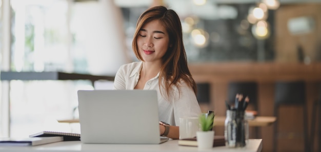 Jeune femme d'affaires travaillant sur son projet tout en utilisant un ordinateur portable dans un lieu de travail confortable