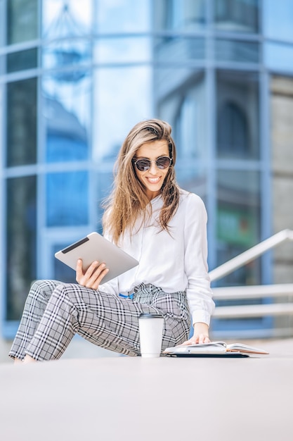 Jeune femme d'affaires travaillant sur la tablette à l'extérieur près du centre d'affaires.