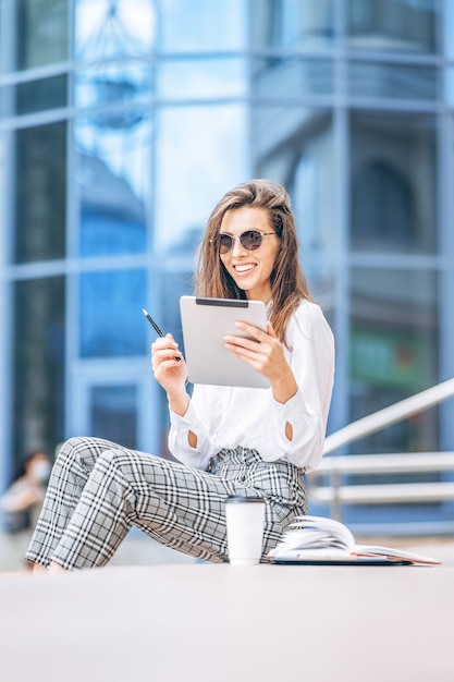 Jeune femme d'affaires travaillant sur la tablette à l'extérieur près du centre d'affaires.