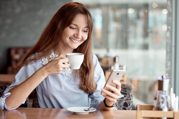 Jeune femme d'affaires utilisant son téléphone intelligent et souriant dans un café.