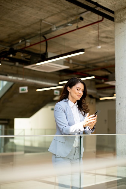 Jeune femme d'affaires utilisant un téléphone portable dans le couloir du bureau