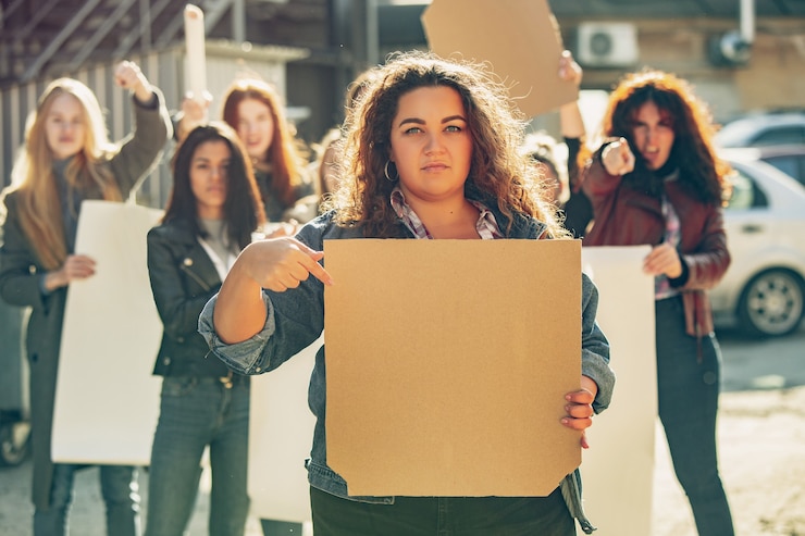 Photo jeune femme avec une affiche vierge devant des personnes qui protestaient contre les droits des femmes et l'égalité dans la rue. réunion sur le problème au travail, la pression masculine, la violence domestique, le harcèlement. espace de copie.