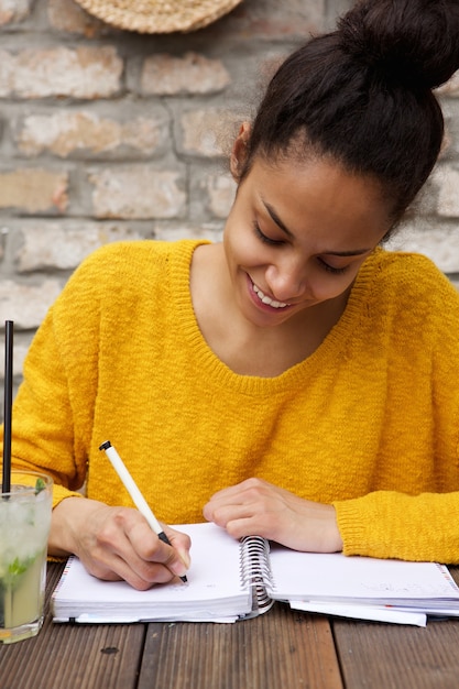 Jeune femme africaine assis à table de café et à écrire des notes