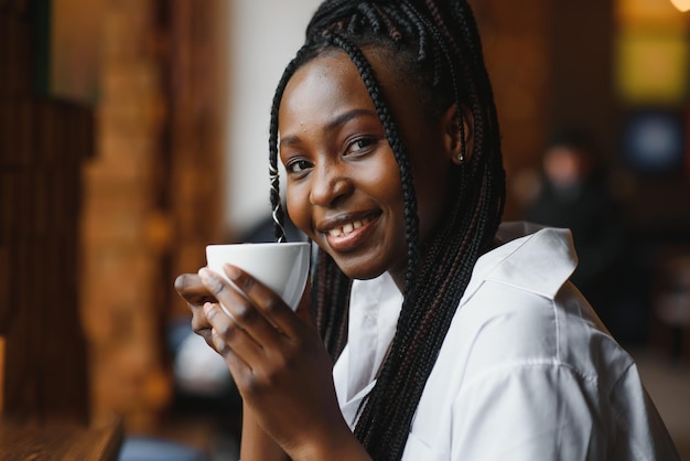 Jeune femme africaine au café buvant du café.