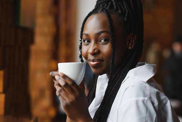 Jeune femme africaine au café buvant du café