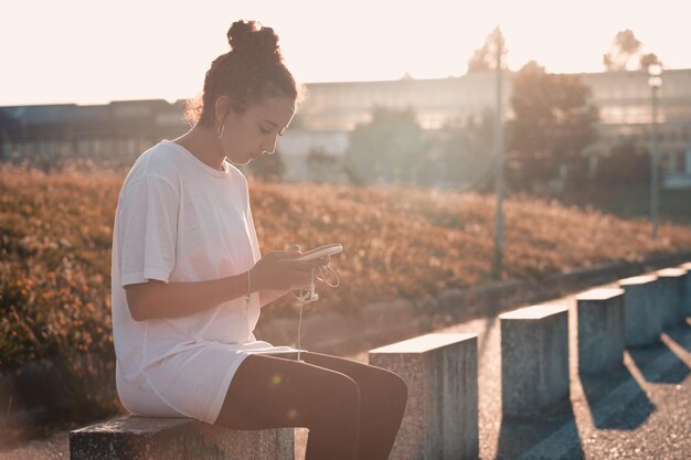 Jeune femme africaine blanche grande soif vérifiant le téléphone après une journée d'exercice assis près de la route