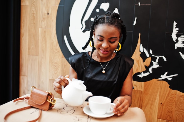 Une Jeune Femme Africaine En Blouse Noire Au Café Boit Du Thé Dans Une Théière.