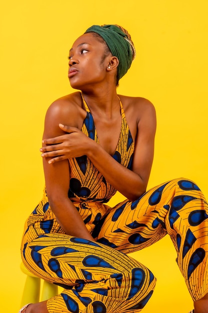 Jeune femme africaine en costume traditionnel sur fond jaune assis en studio