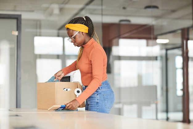 Jeune femme africaine déballant la boîte avec des étoffes, elle obtient un nouvel emploi au bureau