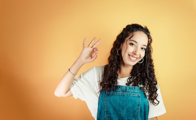 Jeune femme africaine faisant le signe ok à la caméra tout en souriant, arrière-plan de couleur jaune, arrière-plan amovible, réactions et expressions minimales, personne jeune et heureuse