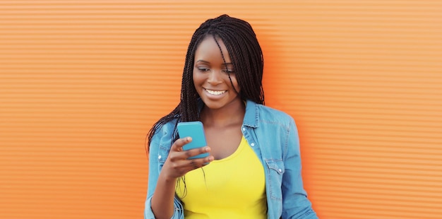 Une jeune femme africaine heureuse avec un téléphone moderne, une fille noire souriante regardant un smartphone en ville.