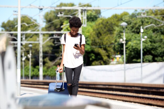 Jeune femme africaine marchant sur la gare avec valise et téléphone portable