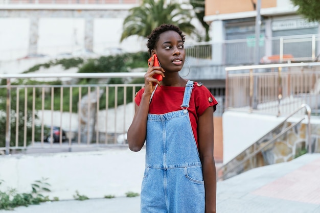 Jeune femme africaine noire parlant au téléphone mobile marchant dans la rue d'une image colorée de ville