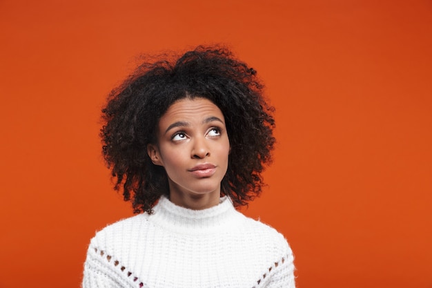 Jeune femme africaine pensive portant des vêtements décontractés, isolée sur un mur rouge