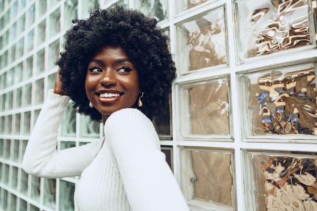 Une jeune femme africaine qui a l'air heureuse en posant contre un mur de verre