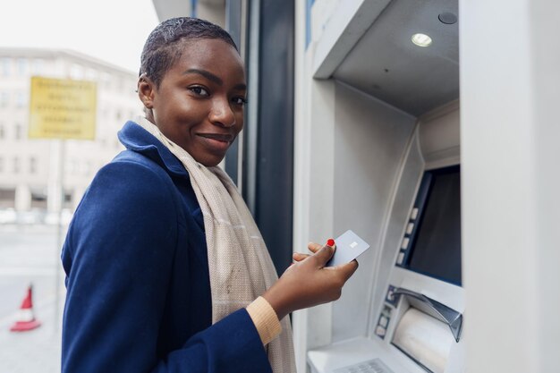 Jeune femme africaine retirant de l'argent au guichet automatique