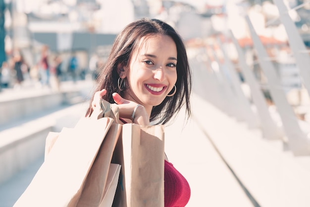 Jeune femme africaine avec des sacs à provisions utilisant un téléphone portable pour passer un appel en marchant sur le centre commercial. Style tendance. Achats et achats personnels consumérisme, vente, achats, shopping, concept de style de vie.