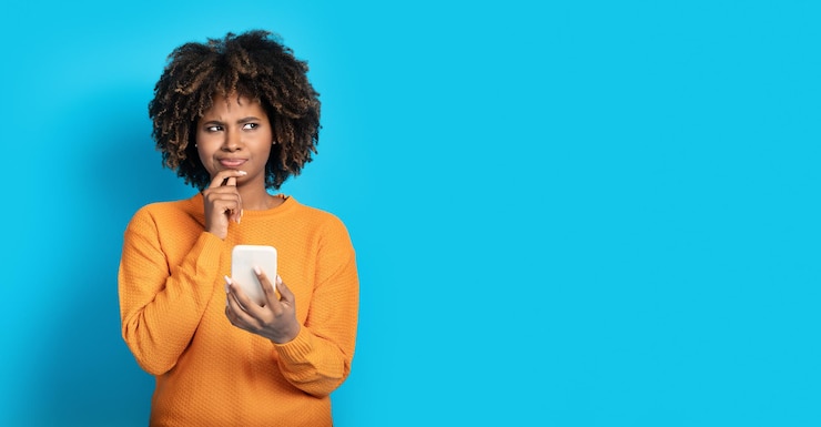 Photo jeune femme africaine sceptique avec téléphone regardant l'espace de copie