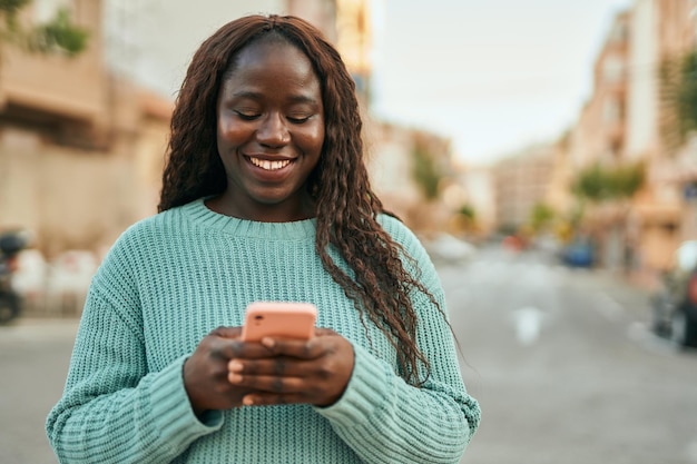 Jeune femme africaine souriante heureuse à l'aide de smartphone à la ville