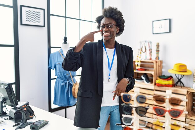 Jeune femme africaine travaillant comme directrice dans une boutique de détail pointant avec le doigt de la main vers le visage et le nez souriant concept de beauté joyeux