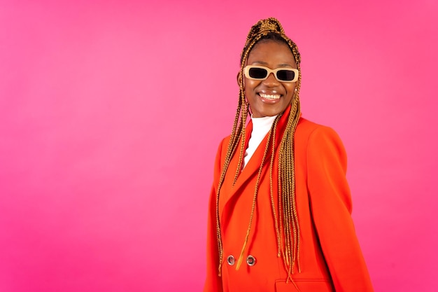 Jeune femme africaine avec des tresses sur fond rose portrait en studio dans un costume rouge et des lunettes de soleil