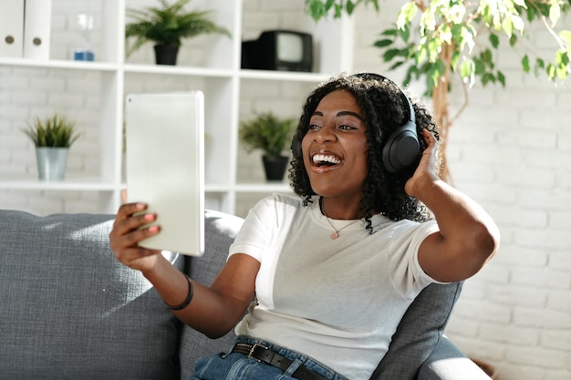 Jeune femme africaine utilisant une tablette numérique et souriant tout en se reposant à la maison