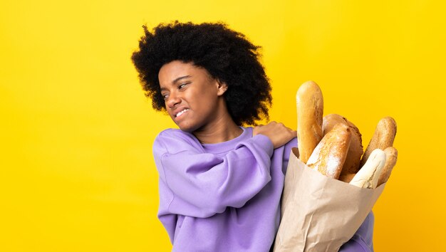 Jeune femme afro-américaine acheter quelque chose de pain isolé sur mur jaune souffrant de douleur à l'épaule pour avoir fait un effort