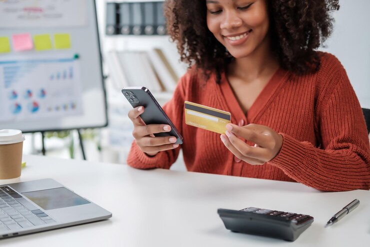 Photo une jeune femme afro-américaine adulte tenant une carte de crédit et un smartphone assise sur le sol à la maison effectuant des transactions bancaires en ligne, du commerce électronique et des achats virtuels.