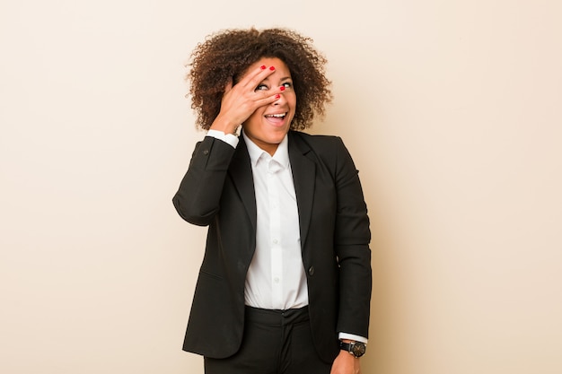 Jeune femme afro-américaine d'affaires cligner des yeux à la caméra à travers les doigts, embarrassé couvrant le visage.