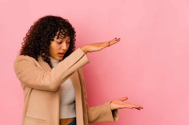 Jeune femme afro-américaine africaine isolée choquée et étonnée tenant un espace de copie entre les mains.