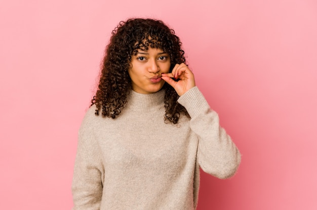 Jeune femme afro-américaine afro-américaine isolée avec les doigts sur les lèvres en gardant un secret.