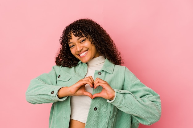 Jeune femme afro-américaine afro-américaine isolée souriant et montrant une forme de coeur avec les mains.